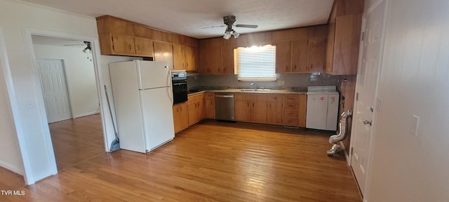 kitchen with sink, stainless steel dishwasher, white fridge, light hardwood / wood-style floors, and black oven