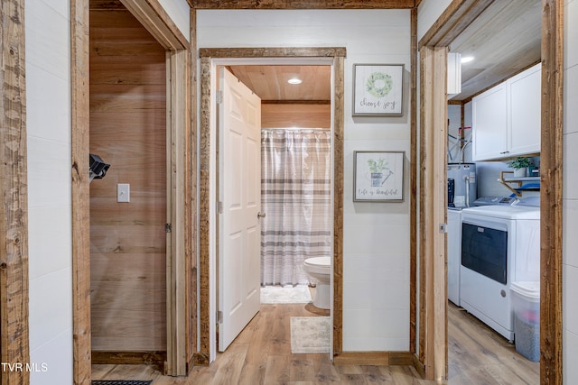 bathroom with water heater, wood walls, toilet, washer and dryer, and hardwood / wood-style flooring