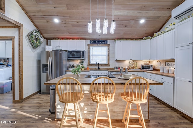 kitchen featuring white cabinetry, stainless steel appliances, a wall unit AC, vaulted ceiling, and a center island with sink