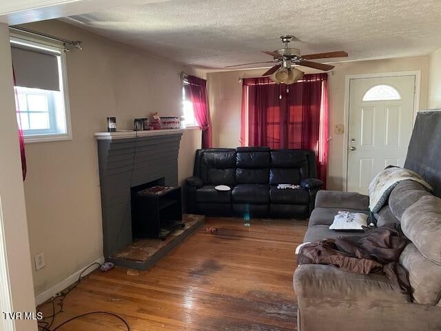 living room with hardwood / wood-style flooring, ceiling fan, a fireplace, and a textured ceiling