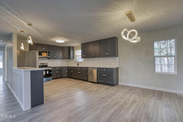 kitchen featuring decorative backsplash, appliances with stainless steel finishes, light hardwood / wood-style flooring, and hanging light fixtures