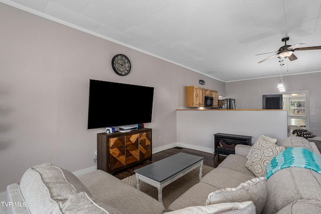 living room featuring ceiling fan, dark hardwood / wood-style flooring, ornamental molding, and a wood stove