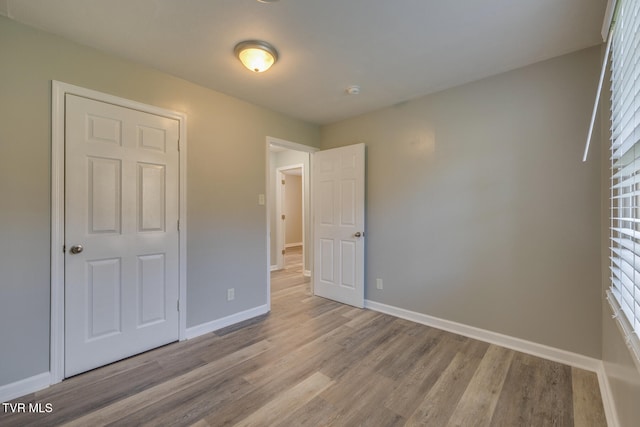 unfurnished bedroom featuring light wood-type flooring, a closet, and multiple windows