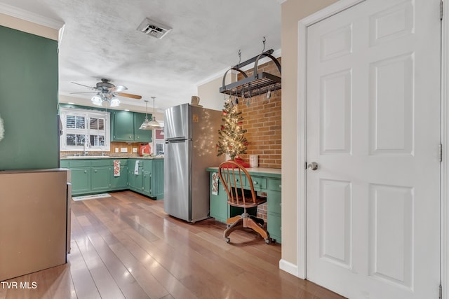 kitchen featuring stainless steel fridge, light wood-type flooring, sink, pendant lighting, and green cabinetry