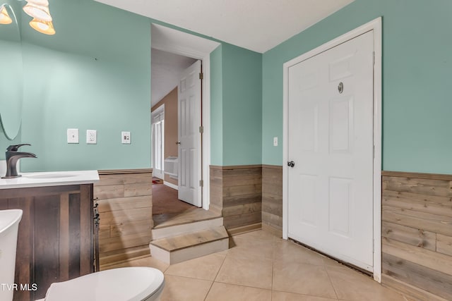 bathroom featuring tile patterned flooring, vanity, toilet, and wooden walls