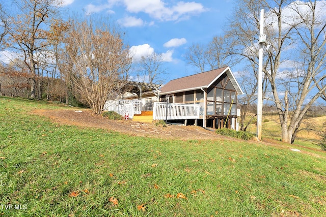 back of property with a wooden deck, a sunroom, and a yard