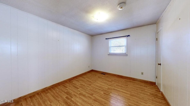 unfurnished room with wood walls, light wood-type flooring, and a textured ceiling