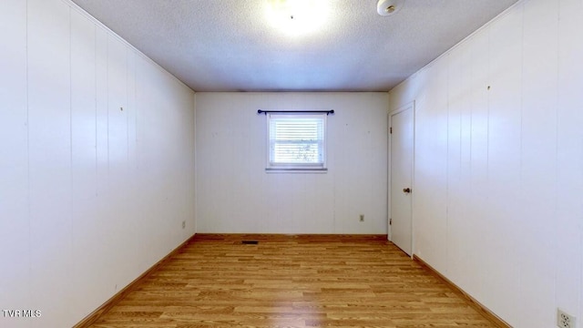 empty room with a textured ceiling, light hardwood / wood-style floors, and ornamental molding