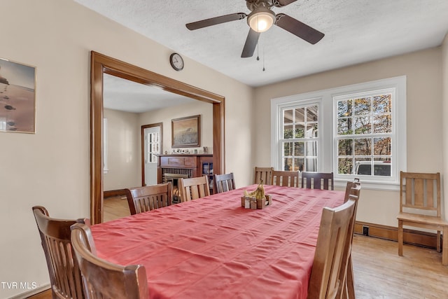 106 W Sycamore Ave, Big Stone Gap, VA 24219 - dining area with light wood-type flooring, ceiling fan, a brick fireplace, a textured ceiling, and baseboards