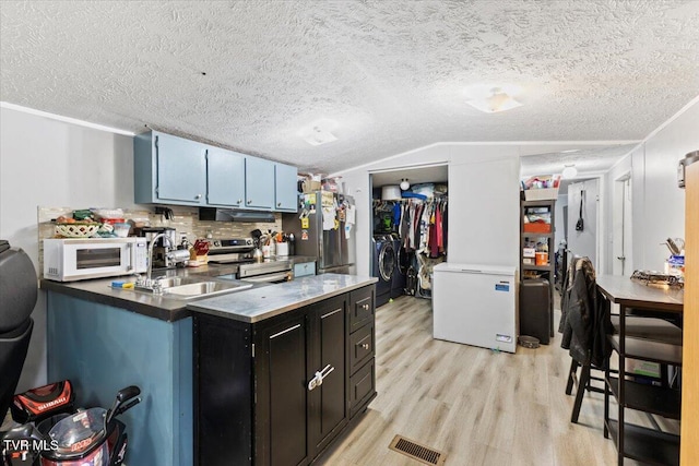 kitchen with stainless steel appliances, a textured ceiling, and light wood-type flooring