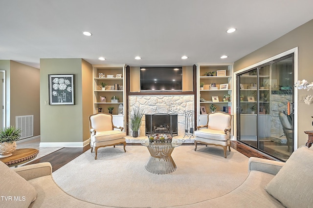 living room featuring built in features, wood-type flooring, and a stone fireplace