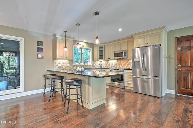 kitchen with kitchen peninsula, appliances with stainless steel finishes, pendant lighting, dark hardwood / wood-style floors, and a breakfast bar area