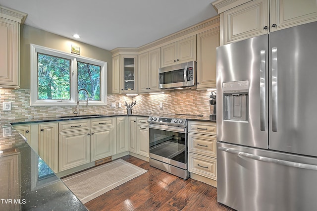 kitchen featuring dark stone counters, stainless steel appliances, dark wood-type flooring, sink, and cream cabinetry