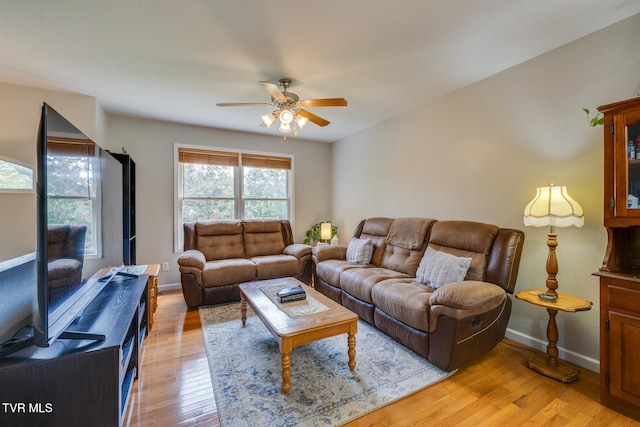 living area with light wood finished floors, a ceiling fan, and baseboards