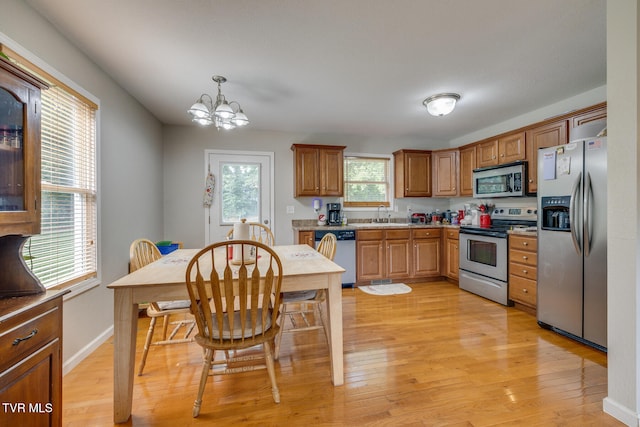 kitchen with light wood finished floors, appliances with stainless steel finishes, brown cabinets, pendant lighting, and a sink