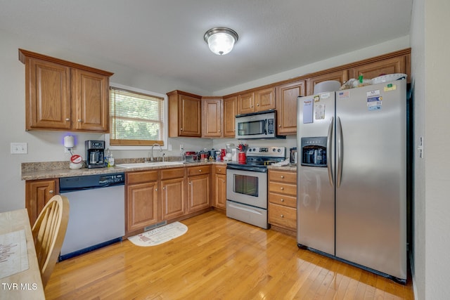 kitchen featuring light countertops, appliances with stainless steel finishes, brown cabinetry, a sink, and light wood-type flooring