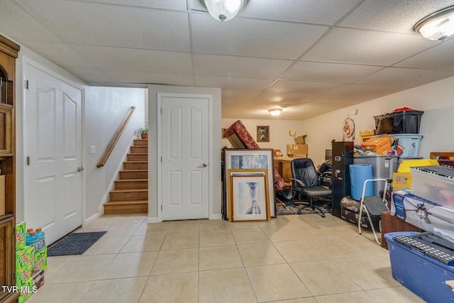 finished basement featuring a drop ceiling, stairway, and light tile patterned flooring