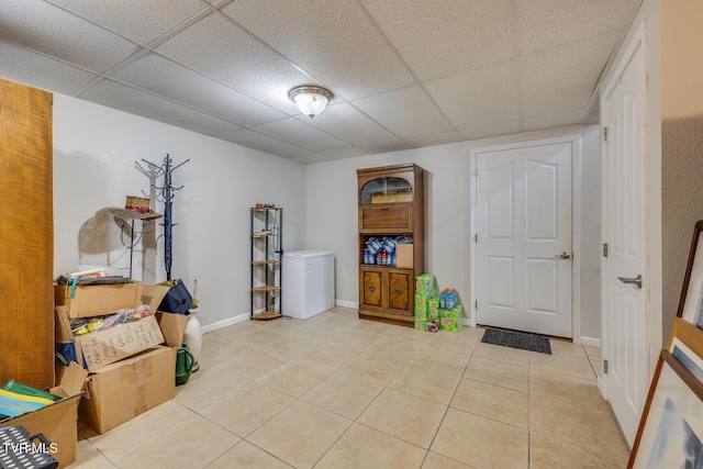 interior space featuring a paneled ceiling, light tile patterned floors, baseboards, and refrigerator