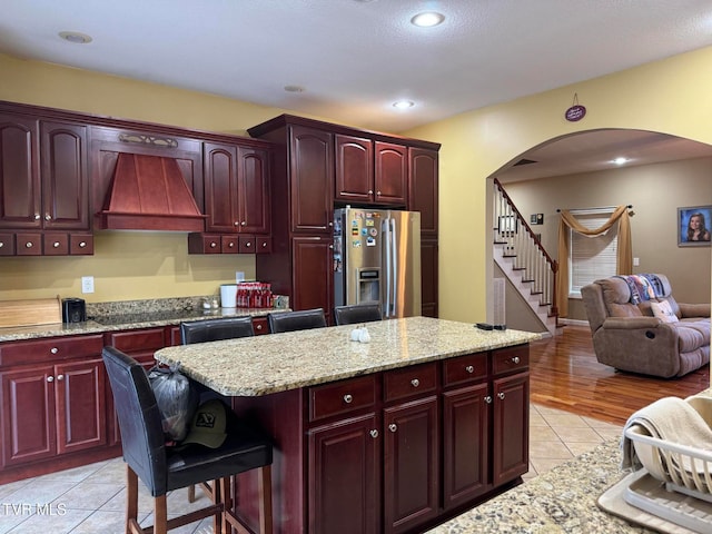 kitchen with light stone countertops, stainless steel fridge, light wood-type flooring, and custom range hood