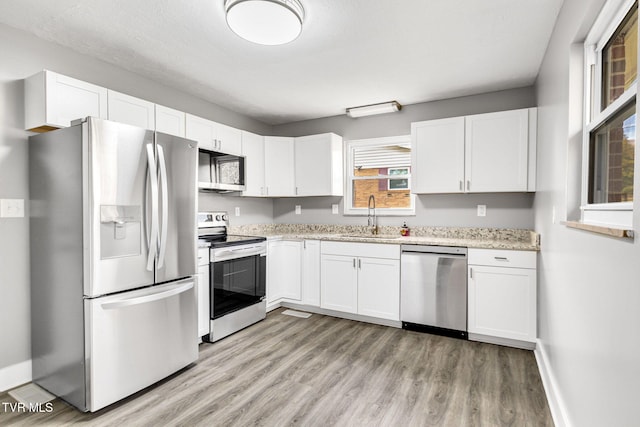 kitchen with appliances with stainless steel finishes, light wood-type flooring, light stone counters, sink, and white cabinetry