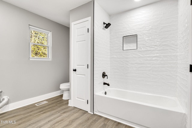 bathroom featuring hardwood / wood-style flooring, tiled shower / bath combo, and toilet