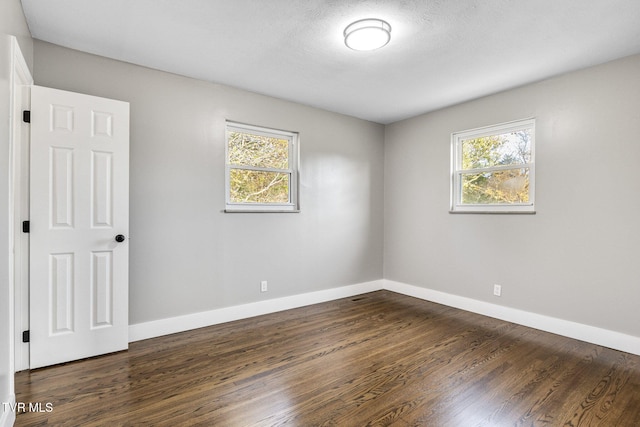 empty room with plenty of natural light, dark hardwood / wood-style floors, and a textured ceiling