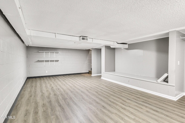 basement featuring light wood-type flooring and a textured ceiling