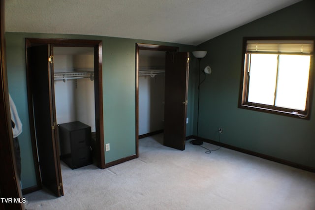 unfurnished bedroom featuring multiple closets, light carpet, and vaulted ceiling