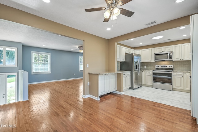 kitchen featuring backsplash, light hardwood / wood-style flooring, white cabinets, and stainless steel appliances