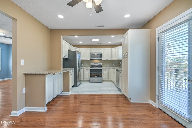 kitchen featuring light stone countertops, appliances with stainless steel finishes, a textured ceiling, light hardwood / wood-style floors, and white cabinetry