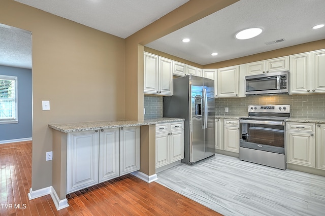 kitchen with light stone countertops, stainless steel appliances, tasteful backsplash, a textured ceiling, and light wood-type flooring