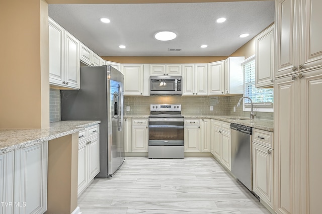 kitchen featuring light stone countertops, appliances with stainless steel finishes, tasteful backsplash, a textured ceiling, and sink