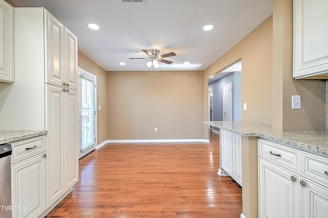 kitchen featuring light wood-type flooring, light stone counters, a textured ceiling, ceiling fan, and white cabinets