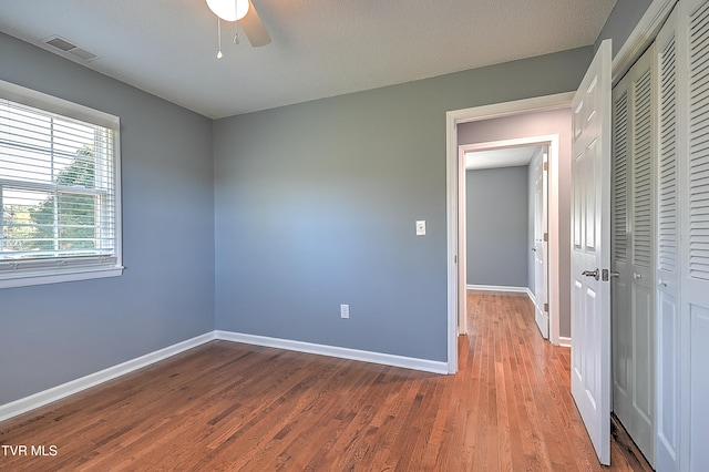 unfurnished bedroom with hardwood / wood-style floors, ceiling fan, a textured ceiling, and a closet