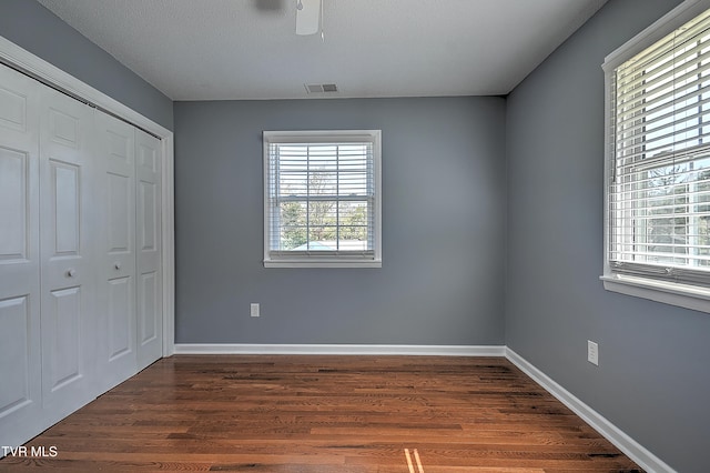 unfurnished bedroom with a closet, multiple windows, ceiling fan, and dark hardwood / wood-style flooring