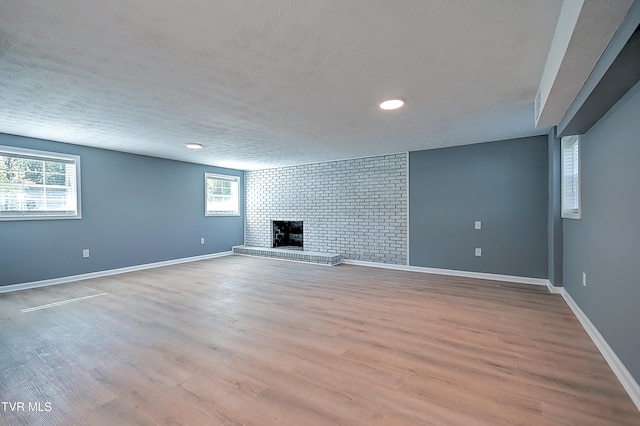 basement with light hardwood / wood-style floors, brick wall, a wealth of natural light, and a brick fireplace