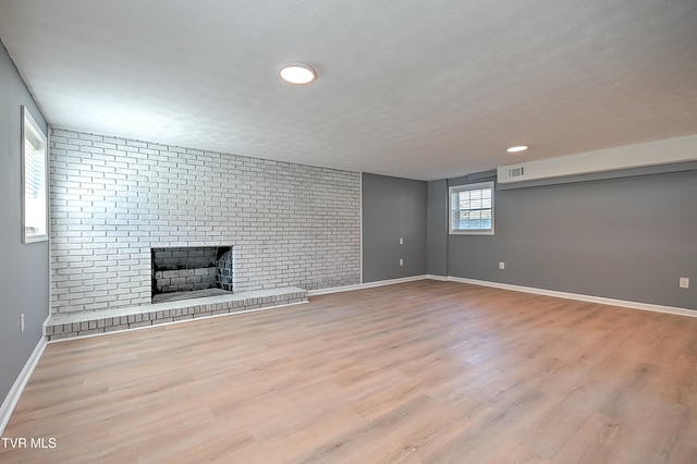 basement featuring brick wall, light hardwood / wood-style floors, a textured ceiling, and a brick fireplace