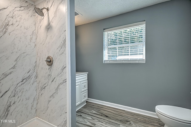 bathroom featuring a tile shower, vanity, a textured ceiling, hardwood / wood-style floors, and toilet