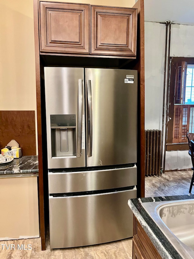 kitchen featuring stainless steel fridge with ice dispenser, dark stone countertops, and radiator heating unit