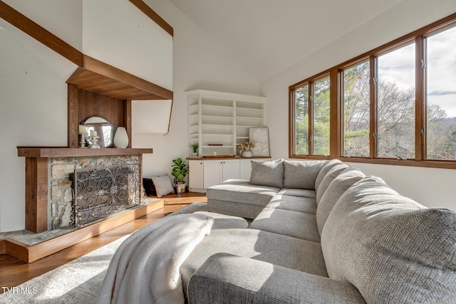 living room featuring a stone fireplace, wood-type flooring, and vaulted ceiling