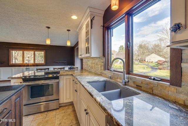 kitchen featuring stainless steel range, sink, light stone counters, pendant lighting, and decorative backsplash