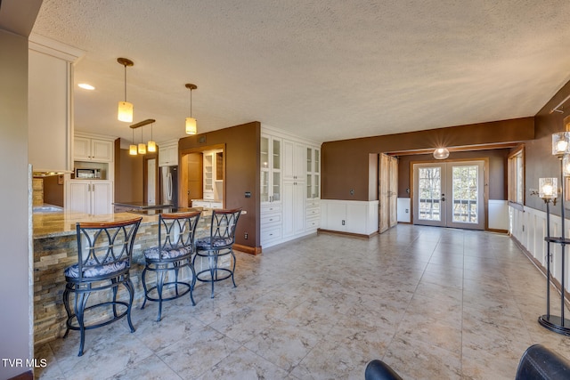 kitchen with french doors, kitchen peninsula, stainless steel fridge, pendant lighting, and a kitchen bar