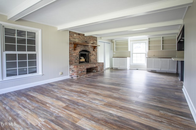 unfurnished living room featuring beam ceiling, dark hardwood / wood-style flooring, a brick fireplace, and crown molding