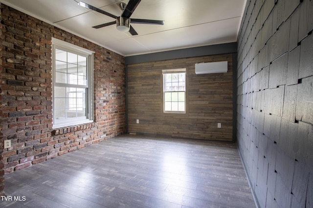 unfurnished room featuring a wall unit AC, ceiling fan, wood-type flooring, and brick wall