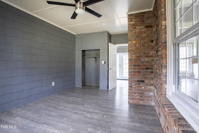 unfurnished room featuring ceiling fan, a wealth of natural light, dark wood-type flooring, and brick wall