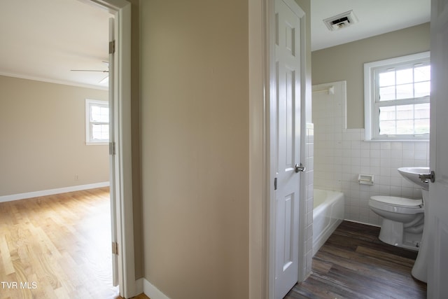 bathroom with ornamental molding, wood-type flooring, tile walls, toilet, and a bathing tub