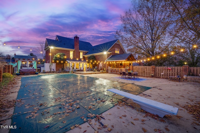 pool at dusk featuring a bar, a diving board, and a patio area