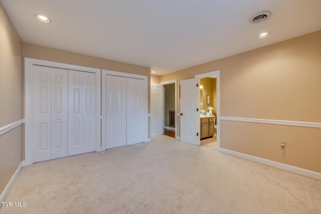 unfurnished bedroom featuring connected bathroom, light carpet, and multiple closets