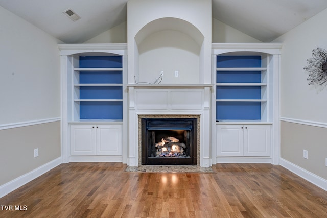 unfurnished living room with built in shelves, vaulted ceiling, and wood-type flooring