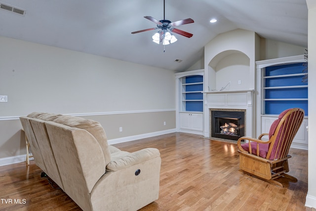 living room featuring a high end fireplace, vaulted ceiling, ceiling fan, built in features, and light hardwood / wood-style floors